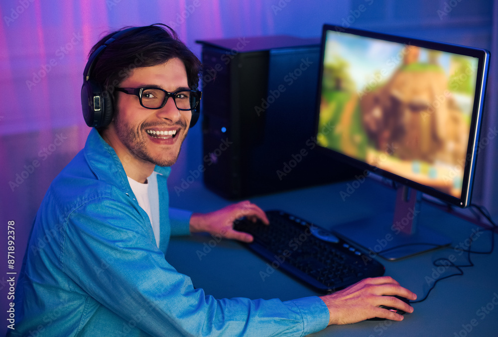 Aufkleber a young man with a blue shirt and headphones plays a video game on a computer at night. he is smilin