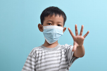 Asian Boy wearing health mask, showing palm with five fingers meaning don't or stop isolated on blue background. Medical and health concept