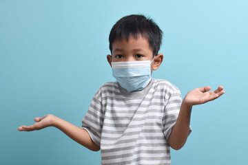 Asian Boy wearing health mask isolated on blue background. Shrugging his shoulders, confused boy looks at the camera. Medical and health concept