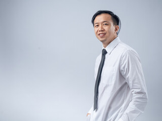 Asian businessman in a white shirt and black tie smiling confidently, standing sideways against a plain light background. The image portrays confidence, professionalism, and success