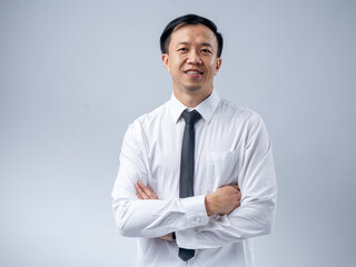 Asian man in a white dress shirt and black tie, standing with arms crossed and smiling confidently....
