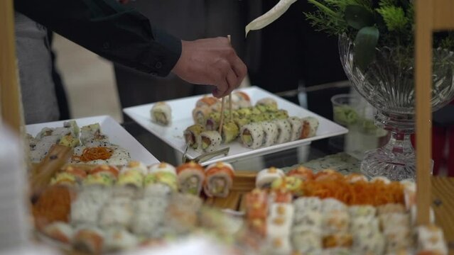 personas escogen su rolls de sushi en una estaci&oacute;n de comida japonesa en una fiesta de bodas