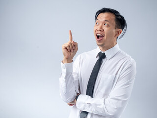 Asian businessman in a white shirt and black tie raising his index finger as if sharing an idea, looking up with an excited expression against a plain light background. The image conveys innovation