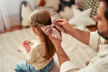 A father ties a bow in his daughters hair, showing a strong bond and affectionate relationship