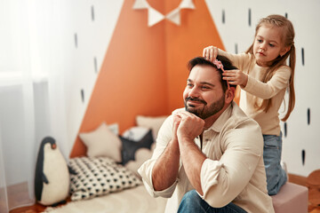 Father and Daughter having fun, child adding hair accessories to her dad in a playroom