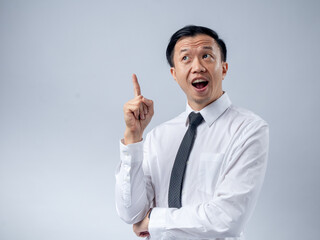 Asian businessman in a white shirt and black tie raising his index finger as if sharing an idea, looking up with an excited expression against a plain light background. The image conveys innovation