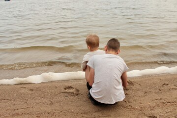 Older brother shows the river to the little kid, two children near the water