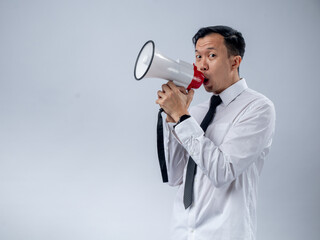 Asian businessman in white shirt and black tie enthusiastically holding a megaphone, speaking or announcing with a joyful expression, standing against a plain light background