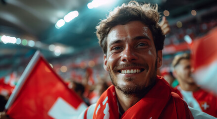 Fototapeta premium Portrait of handsome happy football fan on stadium surrounded with Switzerland flags.