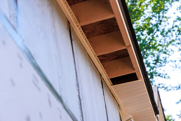 An employee installs soffit on roof corner of house constructed from rafters