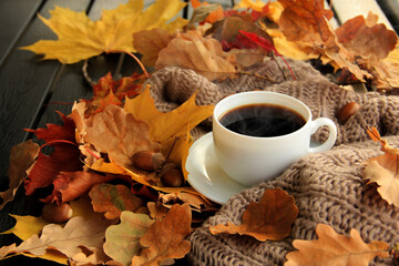 Autumn, fall leaves, hot steaming cup of coffee and a warm scarf on wooden table.  Seasonal, morning coffee, sunday relaxing and still life concept. Selective focus.