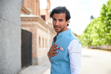 Elegant indian man is posing on a city street, wearing a blue waistcoat and a white shirt