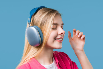 Fototapeta premium Blonde 20s woman listening streaming music, dancing with headphones on blue
