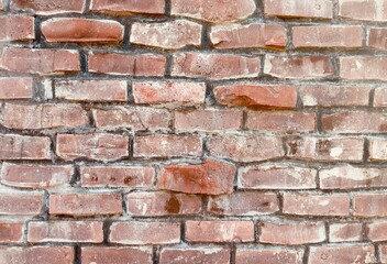 A rustic weathered red brick wall displays a charming, aged look with its worn, textured surface,...