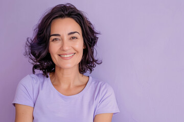 Fototapeta premium A joyful woman with dark curly hair, dressed in a purple shirt against a purple background