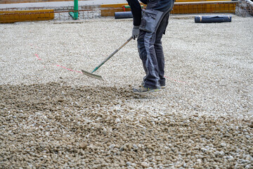 A worker uses a rake to level crushed stone before pouring concrete.