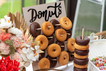 Close-up of chocolate and sugar doughnuts baked on a wooden stand with beautiful dried flowers next to them.