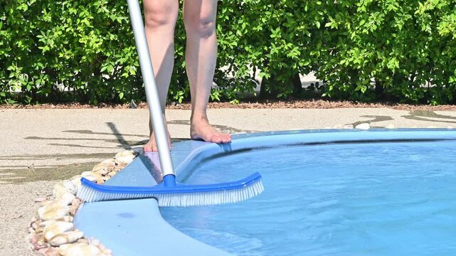 Footage of young housekeeping using a pool brush for cleaning swimming pool.