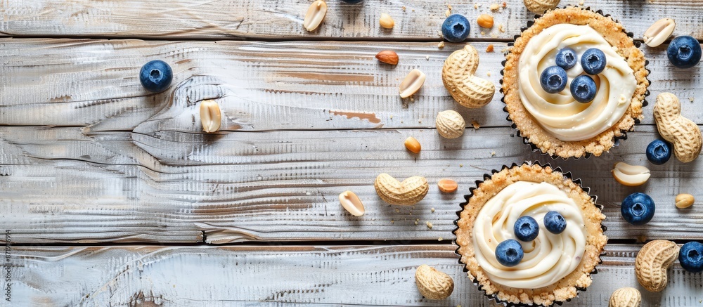 Poster two cheesecakes placed on a light wood background with scattered blueberries and peanuts, suitable f