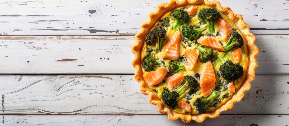 Poster top-down view of a quiche tart containing smoked salmon, broccoli, and spinach on a white wooden bac