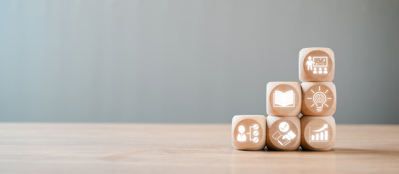 Wooden blocks with icons symbolizing capacity building, education, growth, and development on a wooden table against a neutral background.