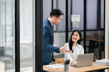 Businessman and businesswoman collaborating in a modern office, discussing work over a laptop, showcasing teamwork and professional interaction.