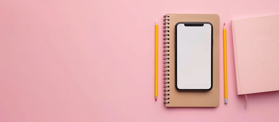 Minimalistic flat lay composition featuring a notebook, pencil, and smartphone on a pink background with ample copy space image.