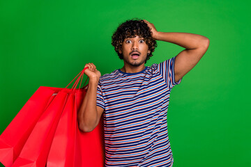 Portrait of young indian curly funny addicted shopaholic with bags man student touch head confused...