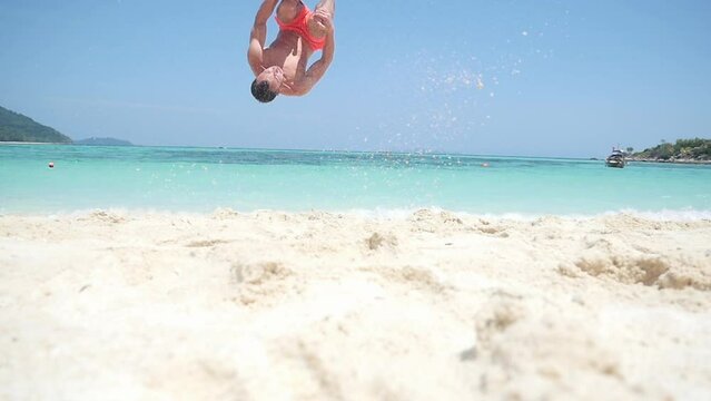 A man does a backlip in slow motion on a heavenly beach in Koh Lipe, Thailand