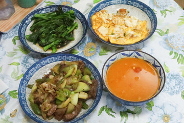 close up top shot of homemade Cantonese Hong Kong style household food with fried egg and tofu, boiled choy sum vegetables, tomato vegetable soup and stir fried celery with beef in blue plates