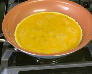 An omelet cooking on a non stick skillet.
