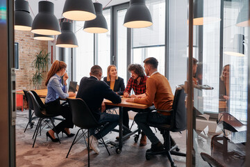 In a sleek glass office space, a team of business professionals engage in lively discussions and exchange strategic ideas, showcasing collaboration and innovation at the heart of modern corporate