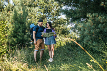 Happy couple tourists with backpacks looking at the map for searching right direction, walking...