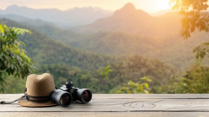 A straw hat and binoculars sit on a wooden table, overlooking a lush mountain valley at sunset