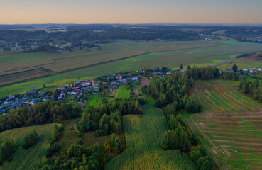 Suburban houses in village, aerial view. Rural landscape at evening sunset. Village wooden house in rural. Roofs of village houses in countryside, drone view. Suburb house at farm field, aerial view.