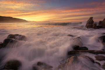 Sunset on Azkorri beach, Getxo with the wakes of the waves between the rocks in the foreground