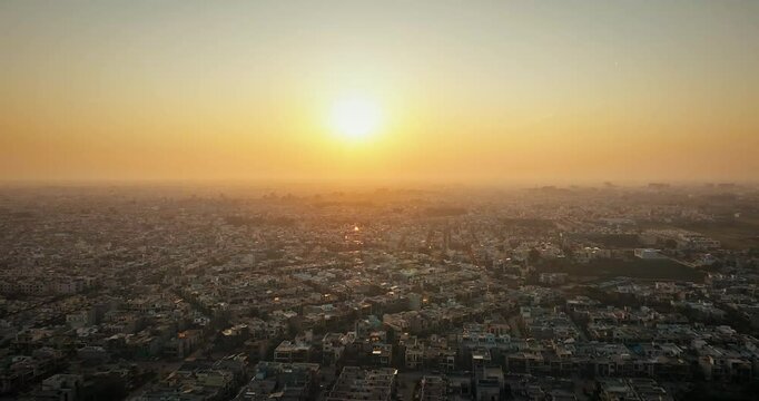 Drone footage of a misty winter sunset over Mohali, Punjab. Warm glow bathes the city as the drone flies toward the setting sun, creating a serene seasonal atmosphere.