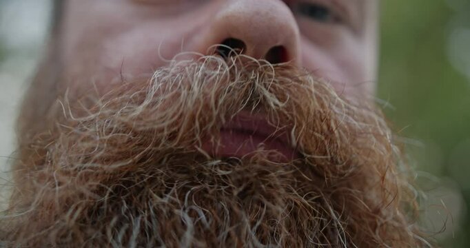 Close-up video shot of a man touching his beard and mustache in an outdoor setting, highlighting facial hair and personal grooming.