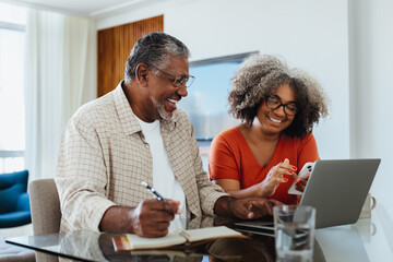 Happy senior couple budgeting at home using laptop and smartphone - Powered by Adobe