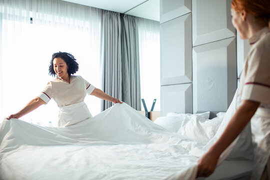 Hotel maids changing bed linens in a bright room