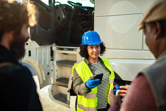 Female logistics manager with clipboard discussing with truck drivers