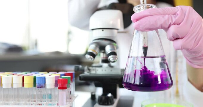 Scientist holds transparent flask with liquid and digs into it purple toxin reagent. Chemical research in laboratory concept