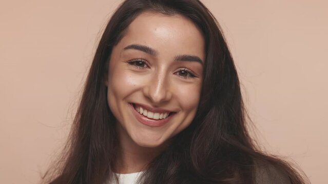 Close-up of a cheerful, winking woman with a radiant smile, expressing happiness and confidence on a plain background.