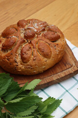 Baked homemade round bread with nettles on a wooden cutting board on wooden table with fresh nettle plants