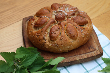 Baked homemade round bread with nettles on a wooden cutting board on wooden table with fresh nettle plants