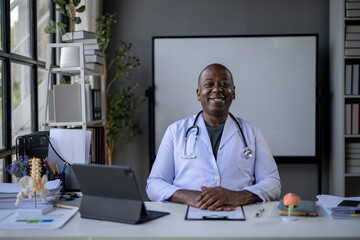 A smiling doctor sits at a desk with a white board behind him