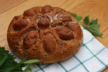 Baked homemade round bread with nettles on wooden table with fresh nettle plants