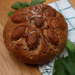 Baked homemade round bread with nettles on wooden table with fresh nettle plants