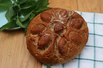 Baked homemade round bread with nettles on wooden table with fresh nettle plants