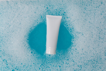 A white tube in blue water with foam. Beautiful streaks on the water. The layout of the cosmetic product.